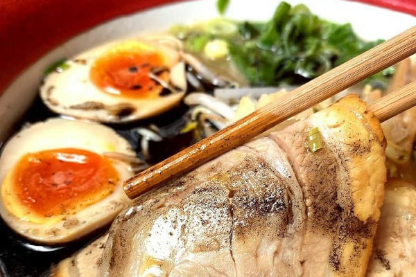 Chopsticks picking up a piece of pork in a ramen dish