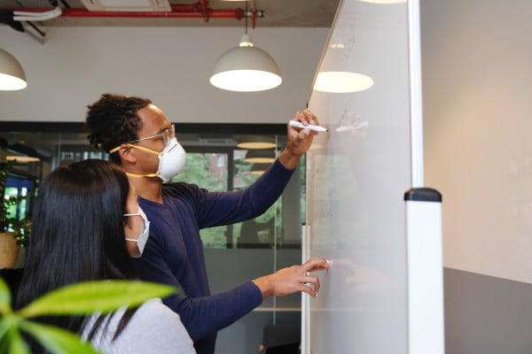 Two people in masks writing on a whiteboard