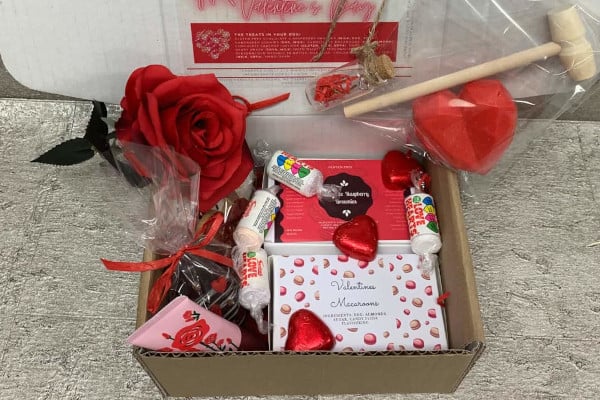 box filled with Valentine's treats like chocolate hearts, roses, hand cream, and macaroons