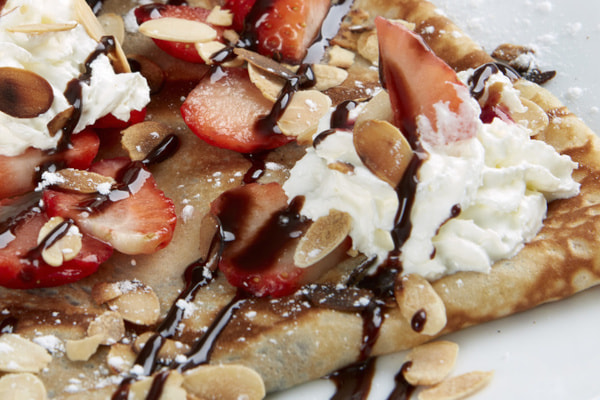 Crepe topped with strawberries, cream, and chocolate sauce