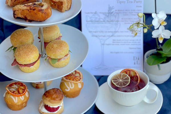 Cakes and sandwiches on an afternoon tea stand next to a cup of tea