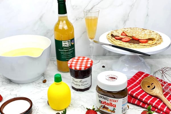 Pancakes on a plate surrounded by toppings and a bottle of juice