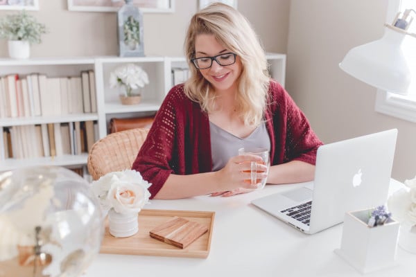 Woman smiling in front on laptop with a drink