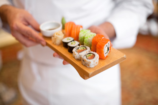 Sushi chef holding out a platter of sushi