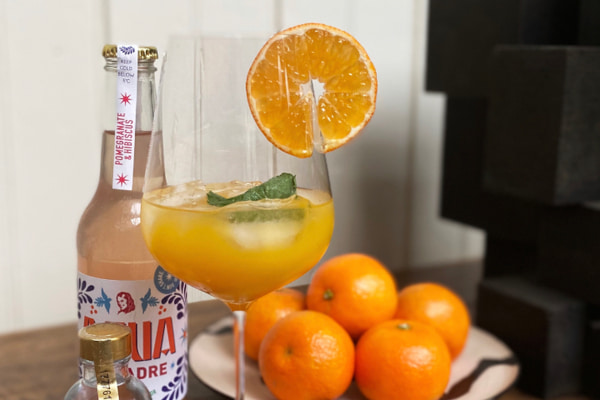 agua de madre bottle next to orange mocktail and oranges