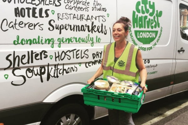 City Harvest volunteer holding green crate of food in front of City Harvest branded van