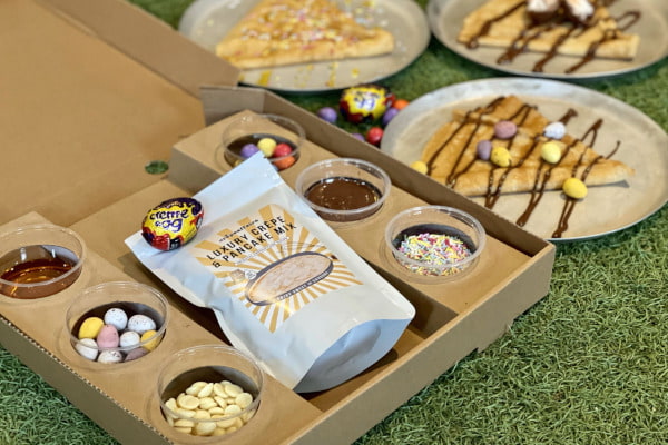 box which contains pancake mix and toppings, next to plates with pancakes on