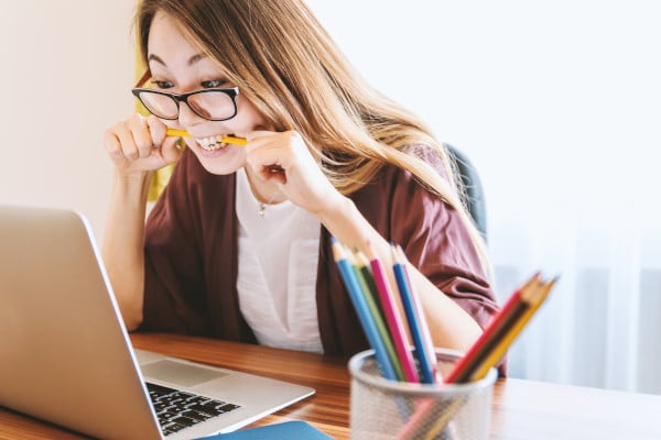 Person biting pencil nervously while looking at laptop scree