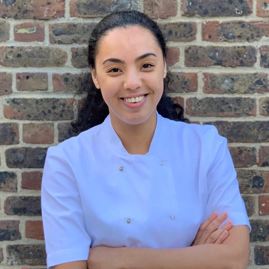Photo of Tamsin Robinson in chef's whites, standing in front of brick wall